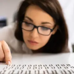Kobieta w okularach z uwagą układa spinacze, co może sugerować kompulsywne zachowania.