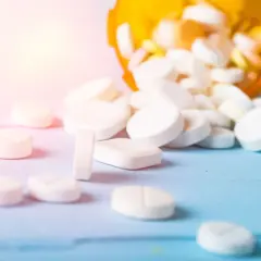 Białe tabletki rozsypane z pomarańczowego pojemnika. Czy to opium? Nie, to leki.