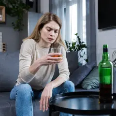 Kobieta z kieliszkiem alkoholu i butelką na stoliku. Obraz symbolizuje 10 strat z picia alkoholu.