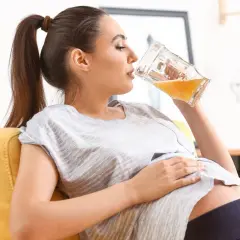Kobieta w ciąży delektuje się piwem bezalkoholowym, siedząc na kanapie.