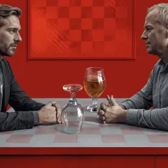 Dwóch mężczyzn siedzi przy stole. Jeden pije piwo, drugi ma pusty kieliszek. Trudne rozmowy o życiu z alkoholikiem niepijącym.