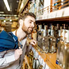 Mężczyzna z brodą wybiera alkohol w sklepie, co może odzwierciedlać spożycie alkoholu w Polsce.