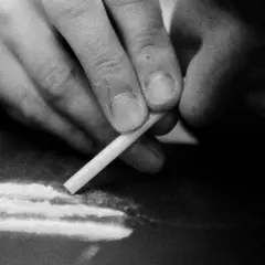 Dłoń przygotowuje kreskę mefedronu, symbolizującą mroczną stronę imprezowania, gdzie alkohol często towarzyszy niebezpiecznym substancjom.