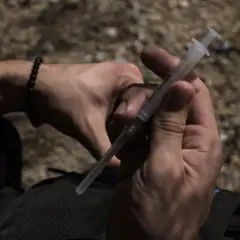 Dłoń trzyma strzykawkę, przygotowując się do podania substancji, która może być niebezpiecznym narkotykiem, znanym jako "Krokodil".