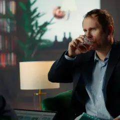 Mężczyzna w garniturze pije whisky, wyglądając na zmęczonego. Czy to obraz wysokofunkcjonującego alkoholika?