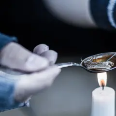 Przygotowanie heroiny do wstrzyknięcia. Łyżka z płynem nad płomieniem świecy, strzykawka w pobliżu.