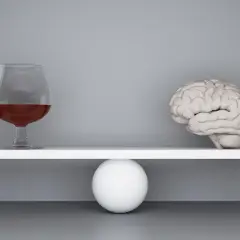 Szalka wagi z mózgiem przechyla się, gdy obok pojawia się kieliszek z alkoholem, symbolizując zmianę zachowania po alkoholu.