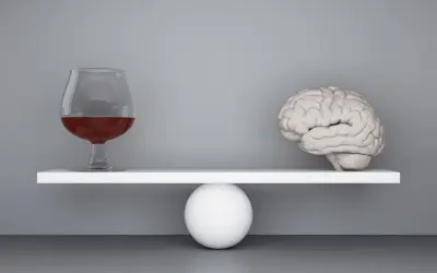 Szalka wagi z mózgiem przechyla się, gdy obok pojawia się kieliszek z alkoholem, symbolizując zmianę zachowania po alkoholu.