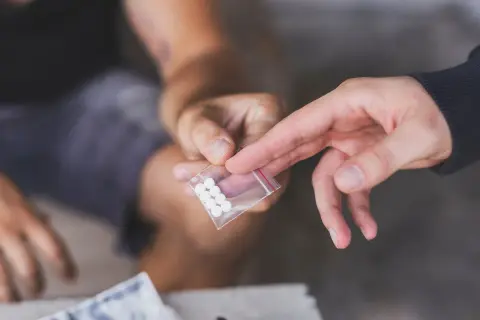 Dwie dłonie przekazują sobie małą torebkę z białymi tabletkami. To może być związane z mdma dawkowanie.