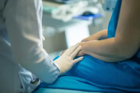 Lekarz w białej rękawiczce delikatnie kładzie dłoń na ramieniu pacjenta w niebieskim ubraniu. To obraz nadziei na przymusowe leczenie narkomana.