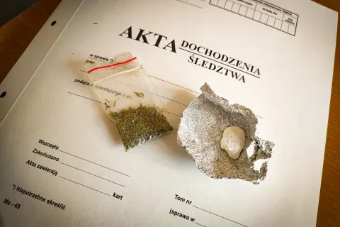 Mała torebka z suszem i grudka substancji w folii aluminiowej na dokumentach śledczych.