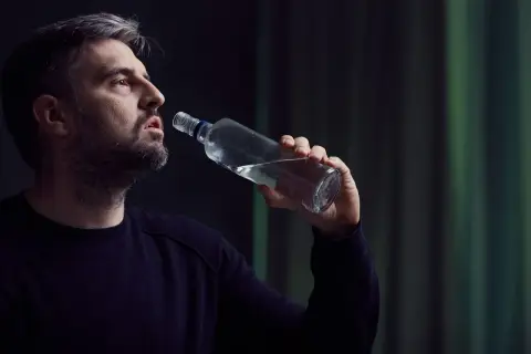 Mężczyzna z siwiejącą brodą pije alkohol z butelki, pogrążony w depresji alkoholowej.