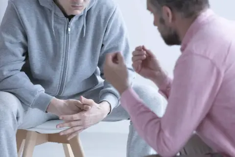 Rozmowa o tym, jak pomóc osobie uzależnionej od narkotyków. Mężczyzna w różowej koszuli wspiera młodego człowieka w szarym dresie.