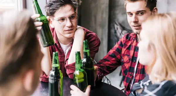 Młodzi ludzie przy stole, butelki piwa, początek alkoholizmu wśród młodzieży.