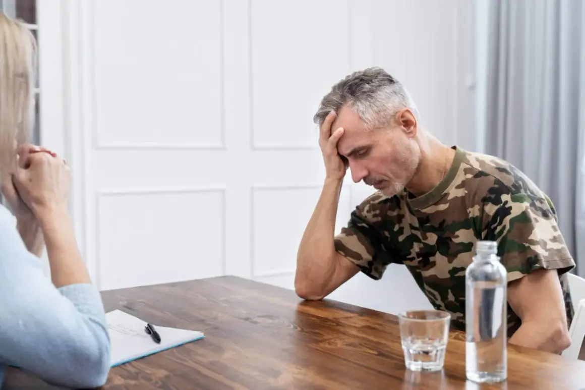 Mężczyzna w mundurze maskującym, z ręką na czole, przeżywa trudne chwile. Rozmowa terapeutyczna, być może przymusowe leczenie alkoholika, jest jego jedyną nadzieją.