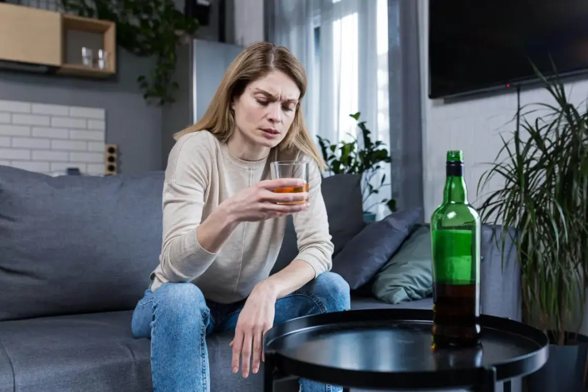 Kobieta z kieliszkiem alkoholu i butelką na stoliku. Obraz symbolizuje 10 strat z picia alkoholu.