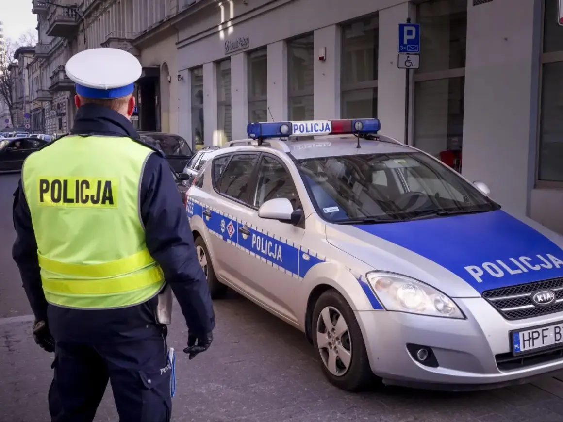 Policjant w kamizelce odblaskowej stoi obok radiowozu z napisem "POLICJA".