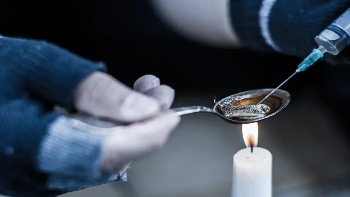 Przygotowanie heroiny do wstrzyknięcia. Łyżka z płynem nad płomieniem świecy, strzykawka w pobliżu.
