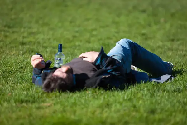 Mężczyzna leży na trawie obok butelki alkoholu, być może doświadczając skutków ubocznych po narkotykach, takich jak drgawki.