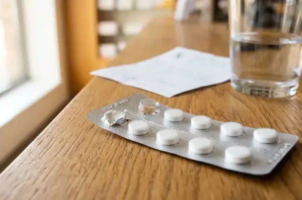Opakowanie tabletek, w tym akamprozat, obok szklanki wody i recepty na drewnianym stole.
