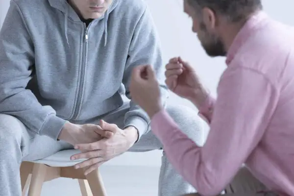 Rozmowa o tym, jak pomóc osobie uzależnionej od narkotyków. Mężczyzna w różowej koszuli wspiera młodego człowieka w szarym dresie.