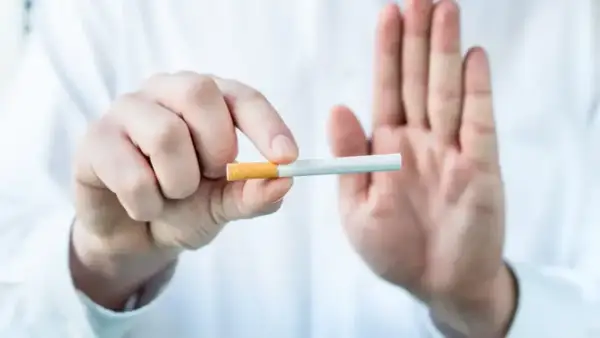 Dłoń trzyma papierosa, druga dłoń pokazuje znak stop. To symbol redukcji szkód i wyboru zdrowszego życia.