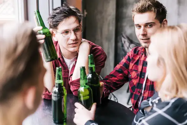 Młodzi ludzie przy stole, butelki piwa, początek alkoholizmu wśród młodzieży.