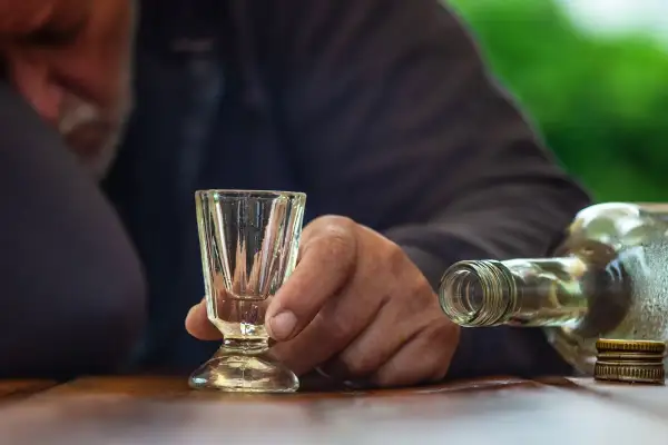 Dłoń trzyma puste kieliszek obok butelki alkoholu.