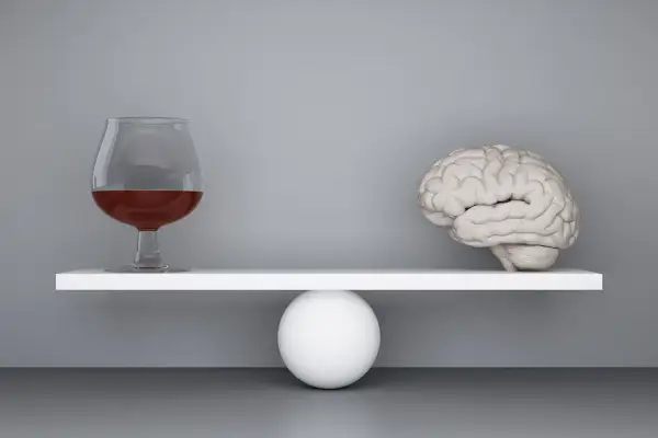 Szalka wagi z mózgiem przechyla się, gdy obok pojawia się kieliszek z alkoholem, symbolizując zmianę zachowania po alkoholu.
