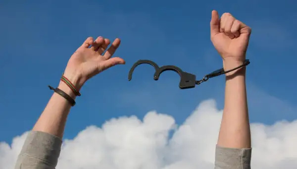 Ręce z rozpiętymi kajdankami unoszą się ku niebu. Symbol wolności po trudnym leczeniu stacjonarnym.